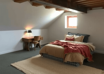 Basement bedroom with low ceiling and exposed beams, featuring a cozy plush bed with layered earth-toned blankets, a worn rug on concrete floor, a reclaimed wood corner desk with a lamp, and a window that lets in soft daylight, creating a serene retreat for relaxation and reflection.